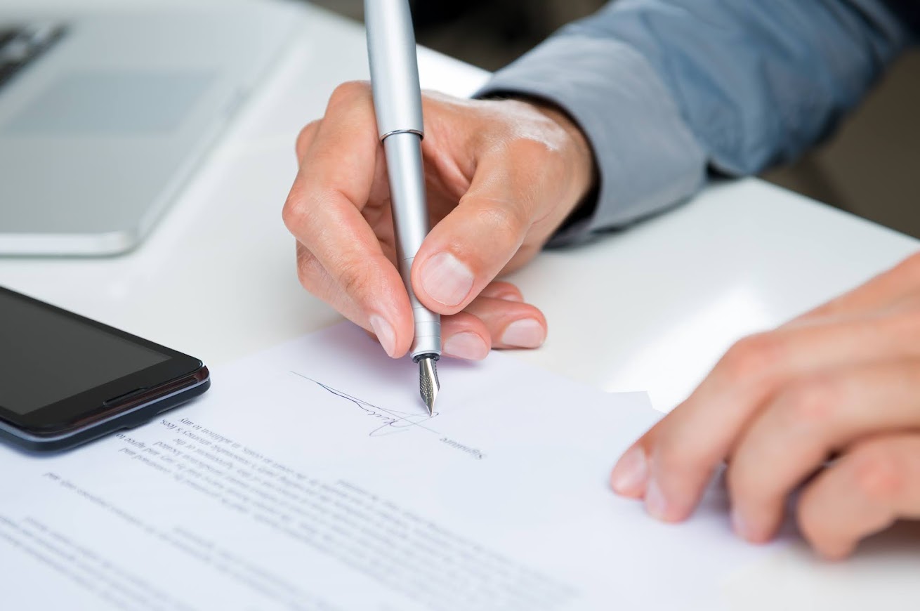 A person signing the document with the pen